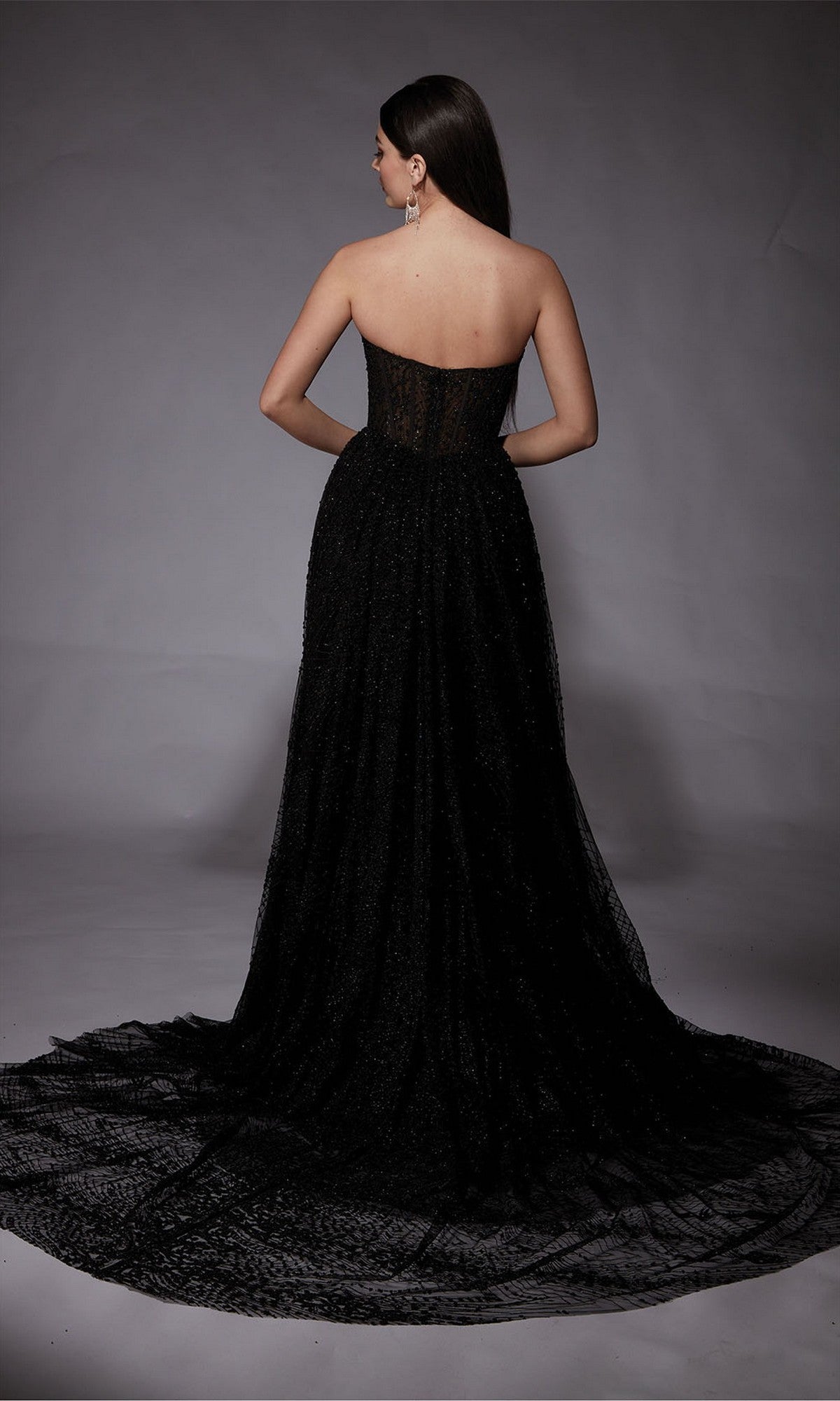 A woman stands facing away against a plain grey background, wearing the Alyce 7133 long formal dress with a strapless neckline and flowing train.